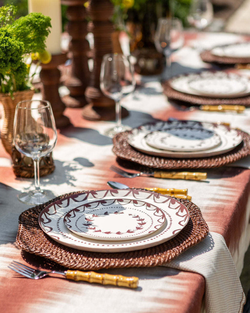 Elegant outdoor table setting with plates, glasses, and cutlery on a patterned tablecloth.