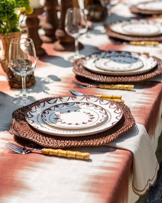 Dining table setting with decorative plates, glasses, and cutlery on a patterned tablecloth.