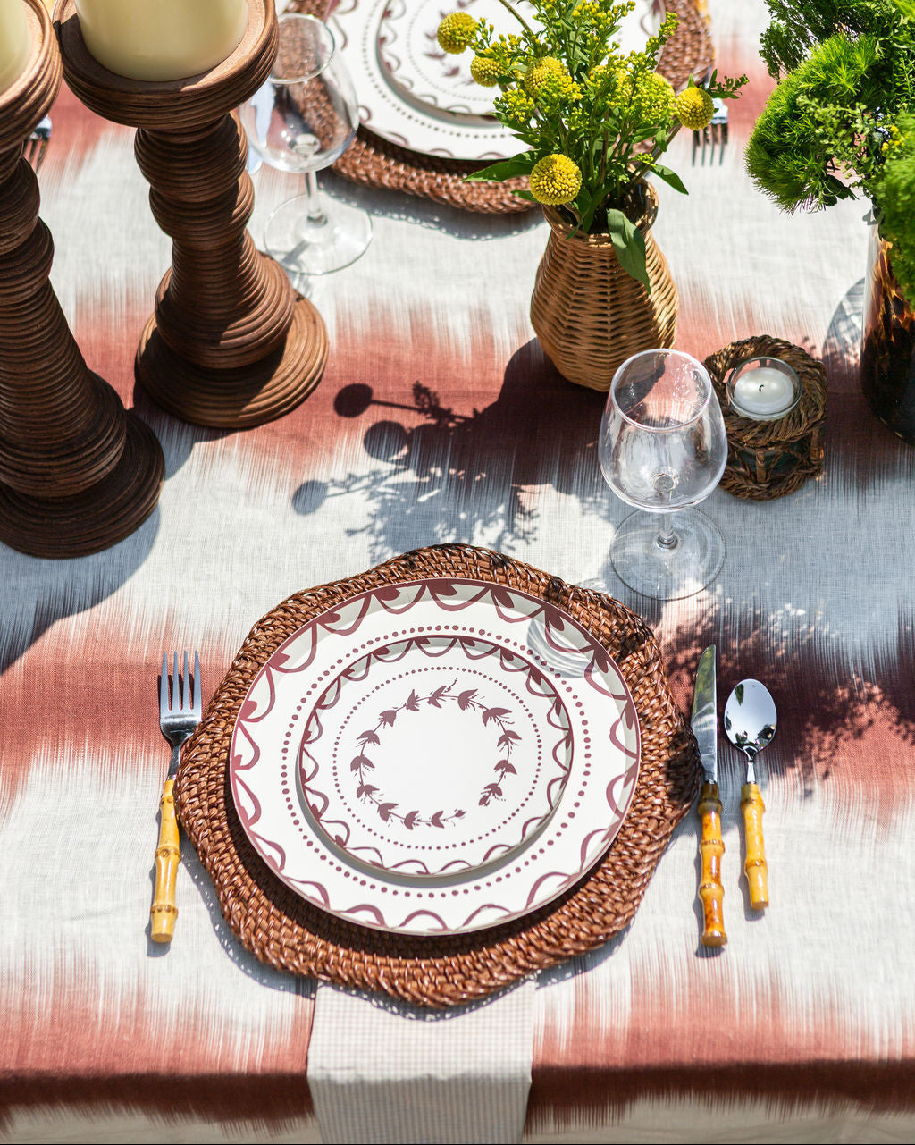 Elegant table setting with decorative plates, cutlery, and candles on a patterned tablecloth.