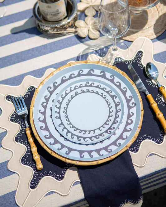 Decorative table setting with a blue and white plate, cutlery, and a bottle on a striped tablecloth.