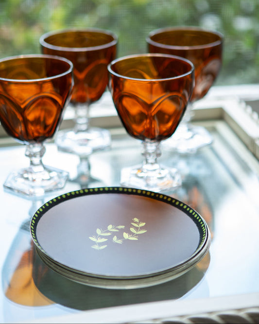Set of amber glass goblets on a reflective surface with a decorative plate.