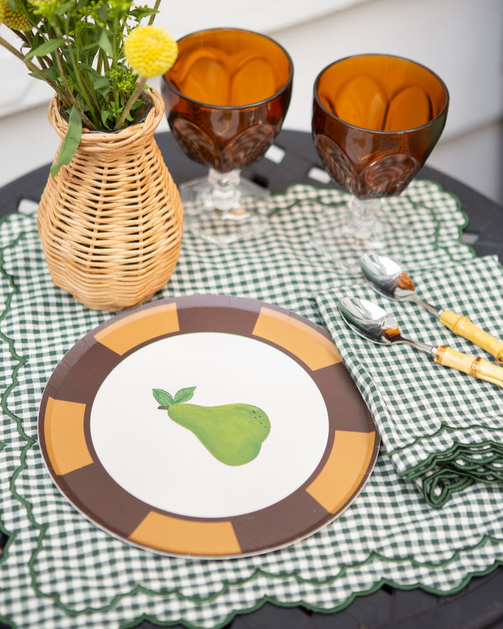 Dining table setting with a plate featuring a pear design, glasses, and cutlery on a checkered placemat