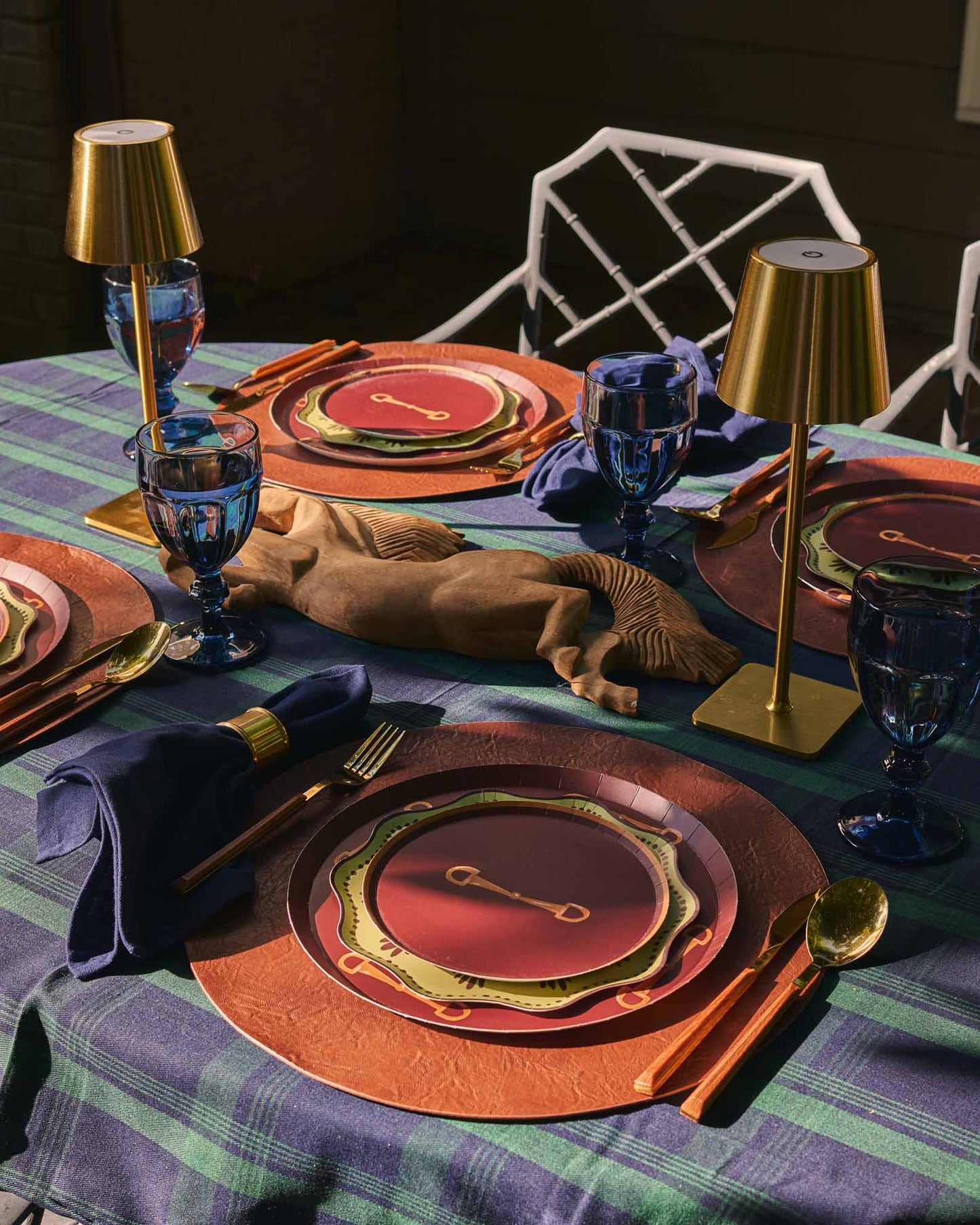 a table setting outdoors with horse themed plates and a blue and green plaidtablecloth