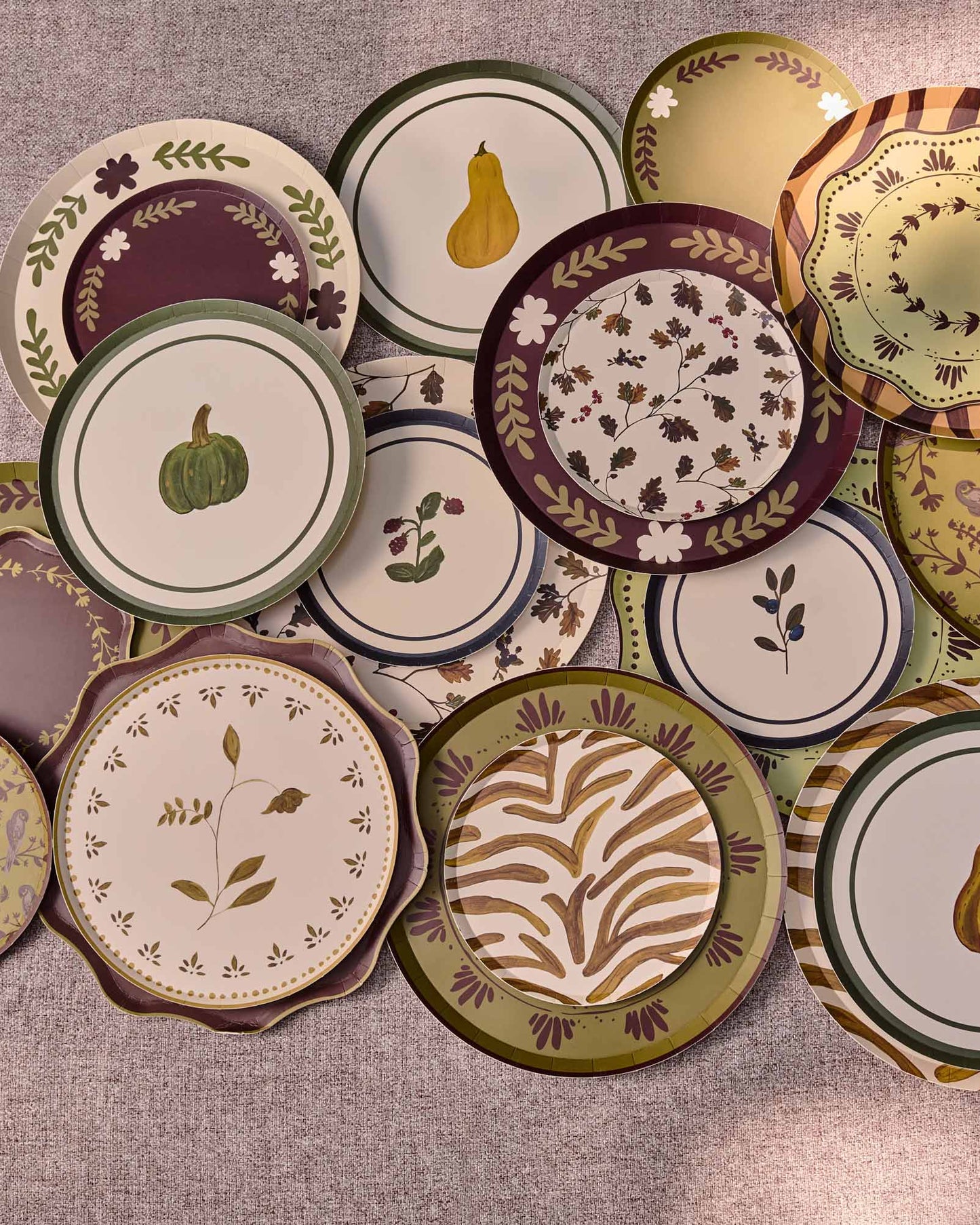 A collection of decorative plates with autumn-themed patterns, including pumpkins, pears, leaves, and floral motifs, arranged on a round gray table.