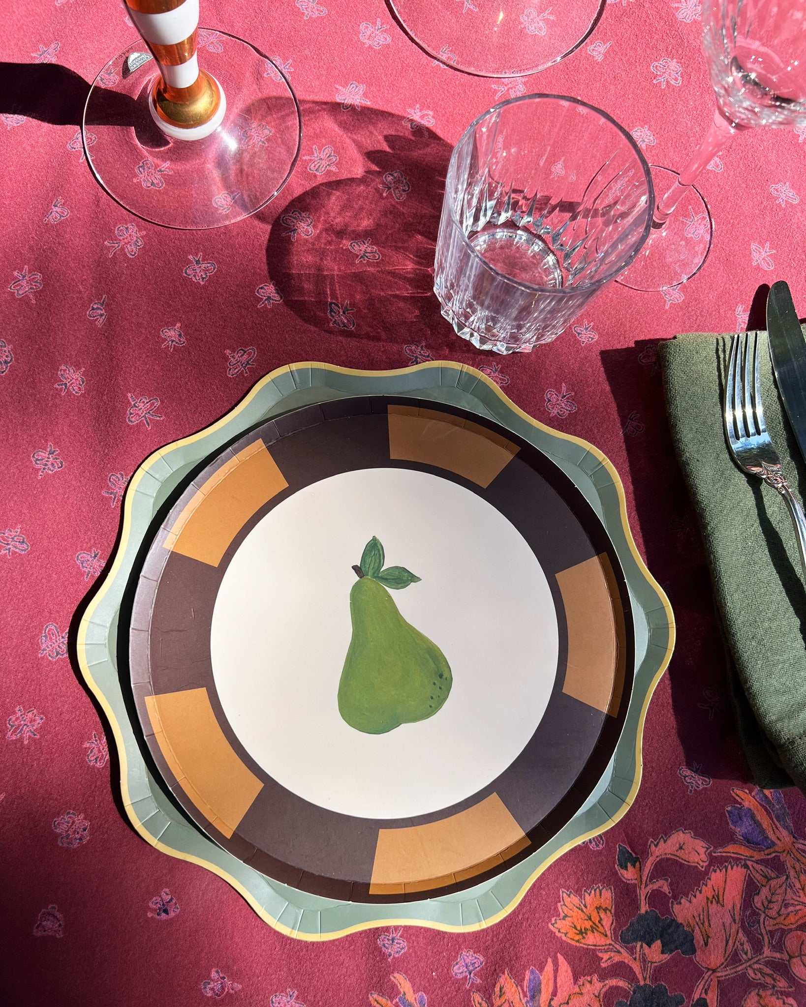 Decorative plate with a pear design on a table with a red tablecloth and glasses.