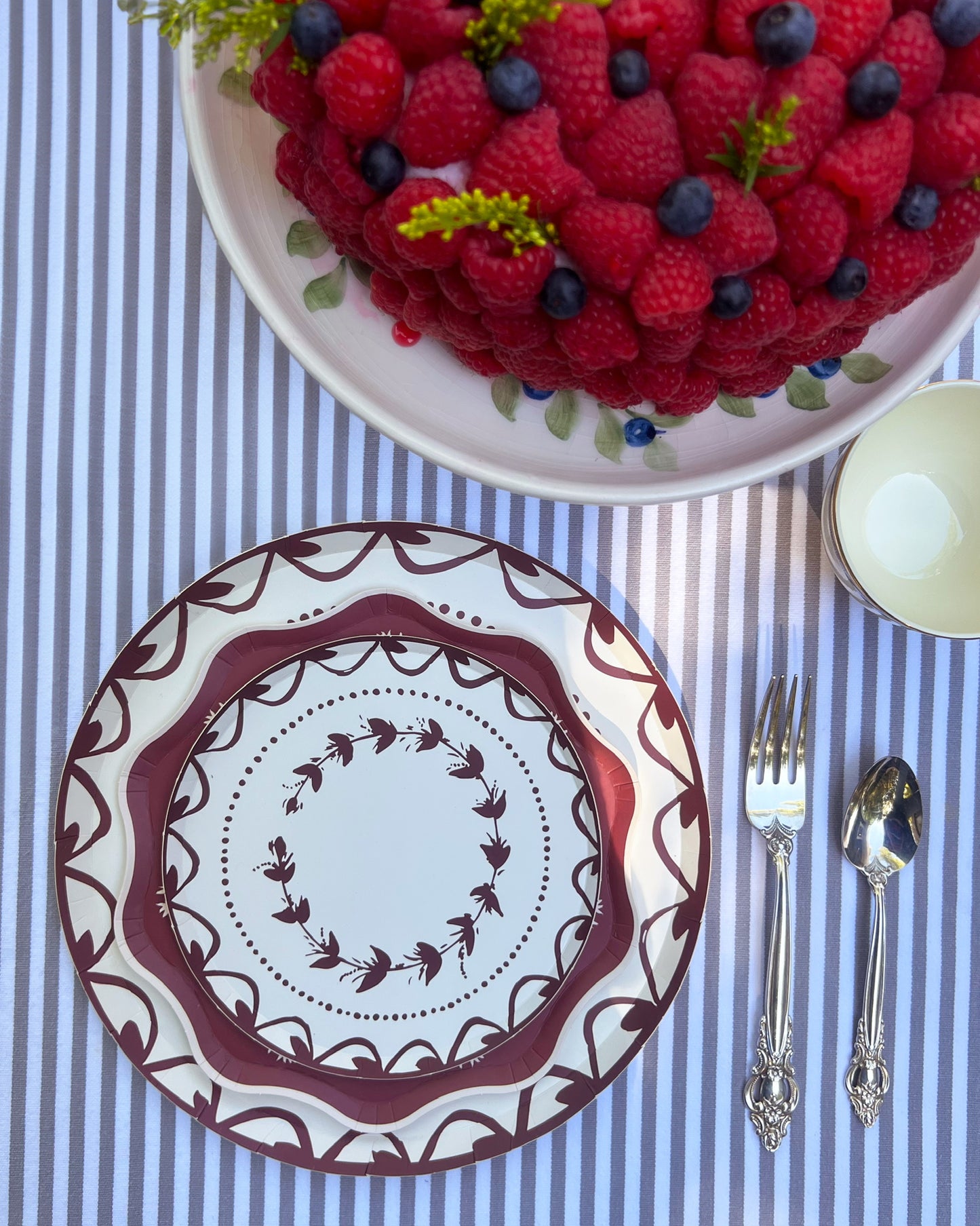 Decorative plate with floral patterns on a table setting with a berry cake and cutlery.