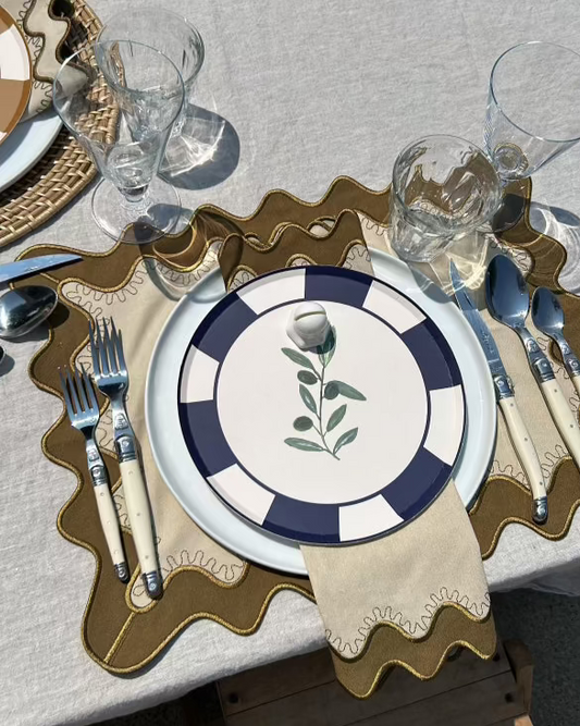 Table setting with a decorative plate, cutlery, and glasses on a textured tablecloth.