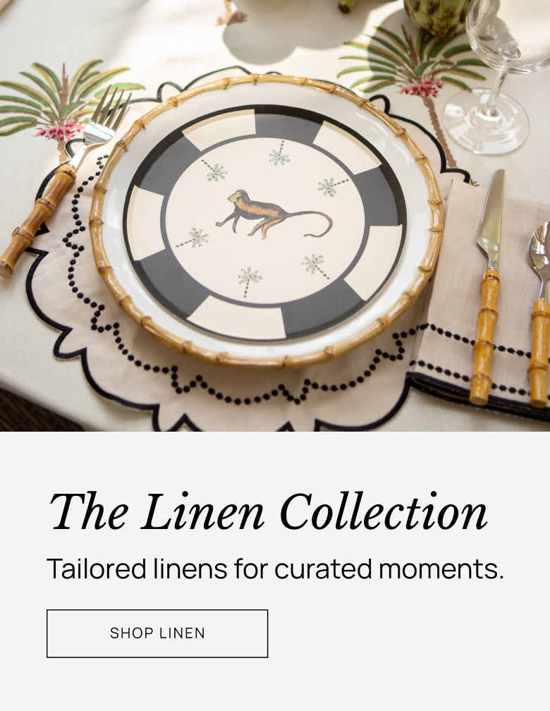 Decorative table setting with a plate featuring a monkey design, surrounded by cutlery and glasses, with 'The Linen Collection' text overlay.
