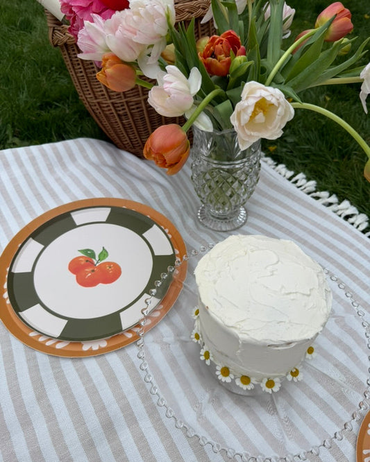 Small white cake on a striped tablecloth with a decorative plate and flowers in the background.