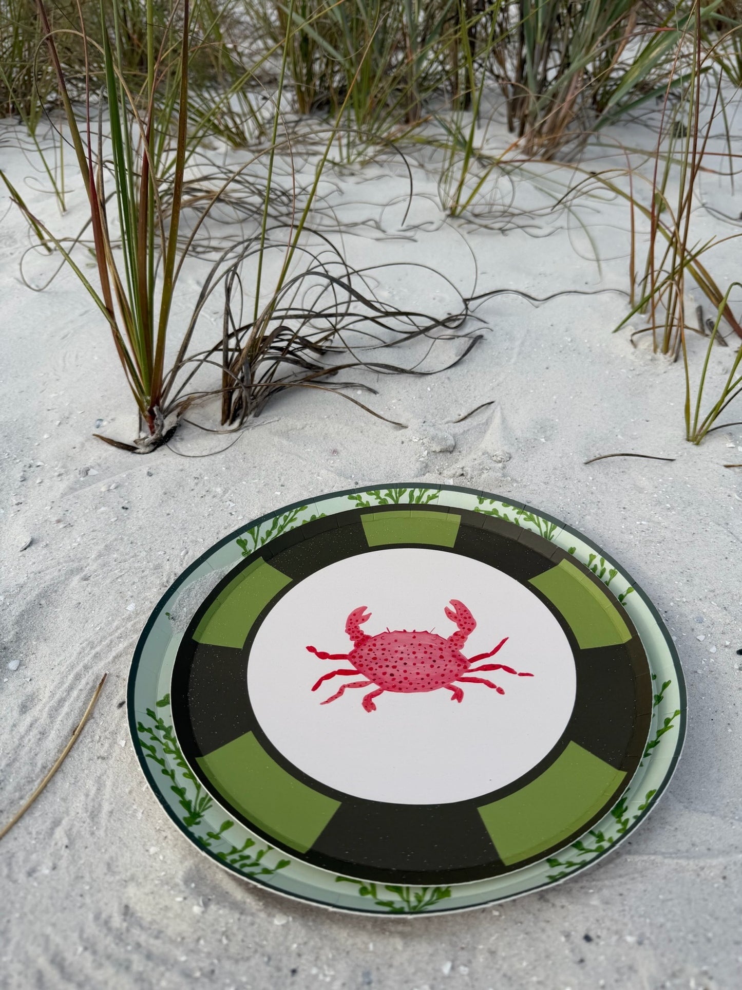 A decorative plate with a crab motif. The plates are laying in the sand
