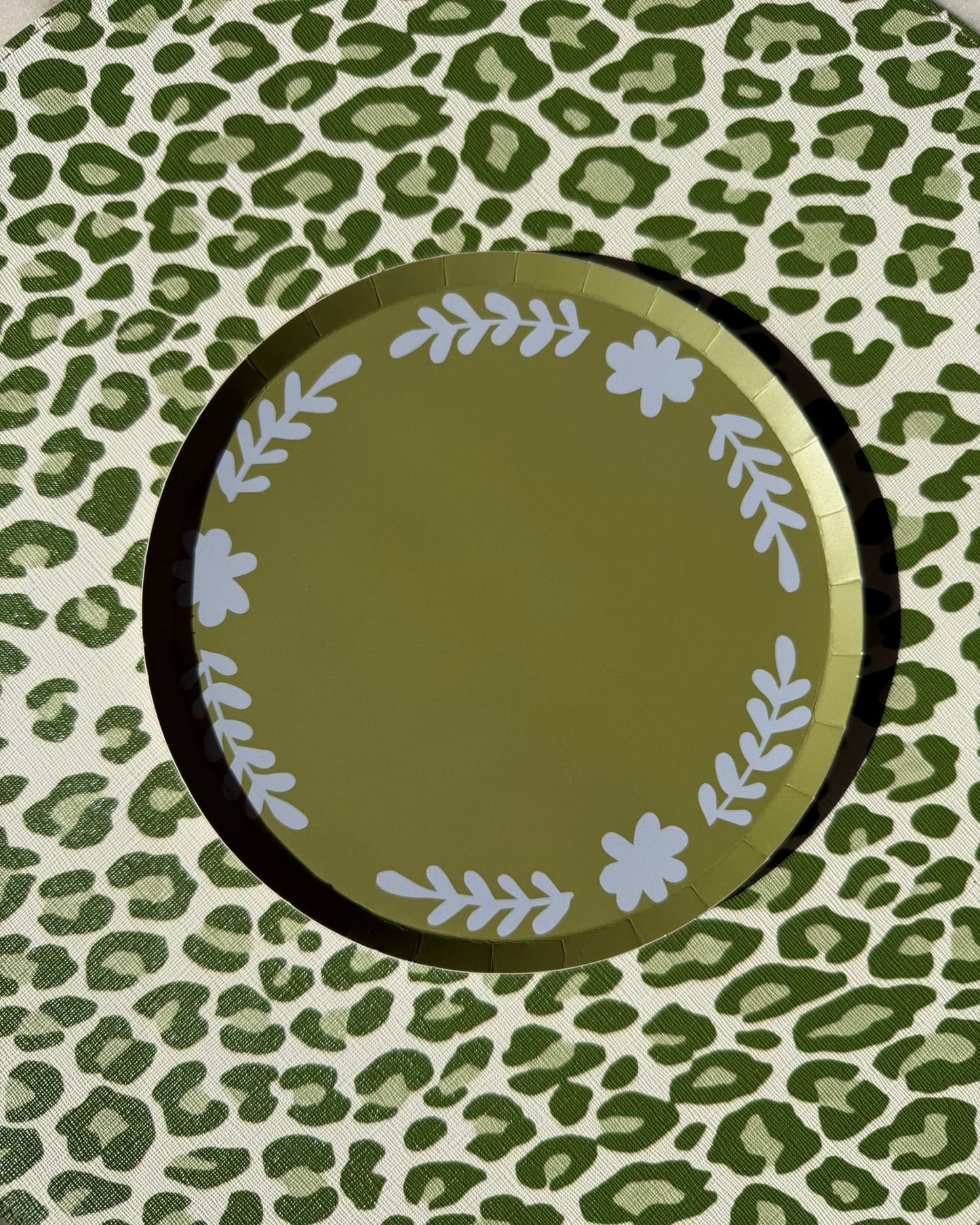 A green plate with floral details on a leopard placemat