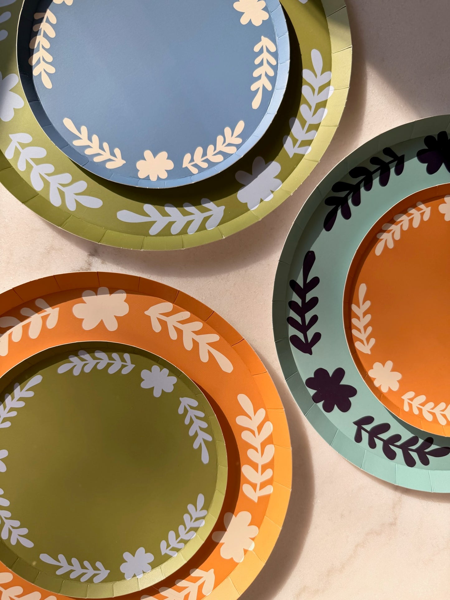 Green, orange and blue plates with a floral boarder stack on top of one another.