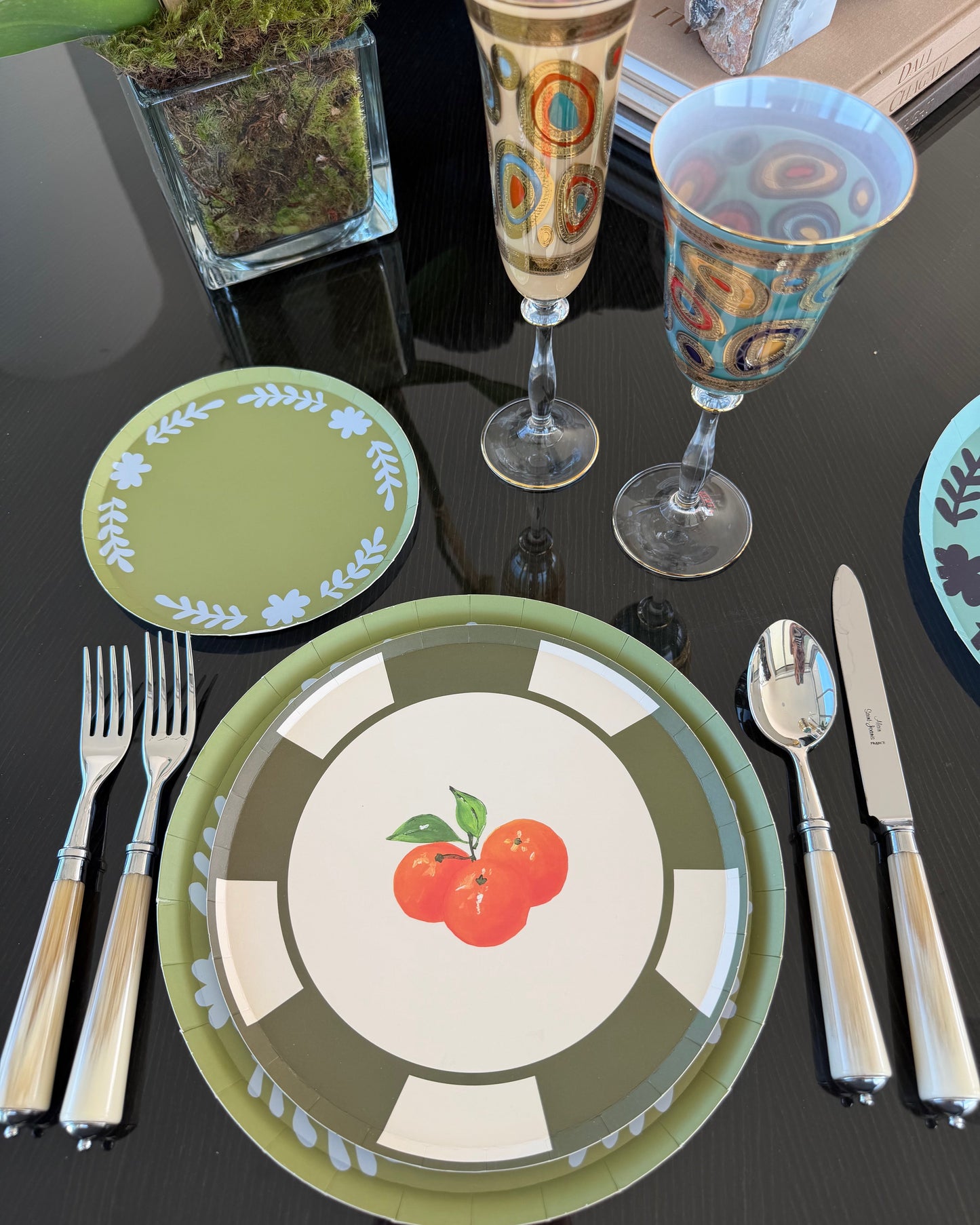 Dining table setting with decorative plates, glasses, and cutlery on a black surface.