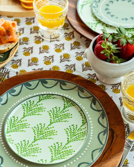 Table setting with a decorative plate, glasses of orange juice, and a bowl of strawberries on a patterned tablecloth.