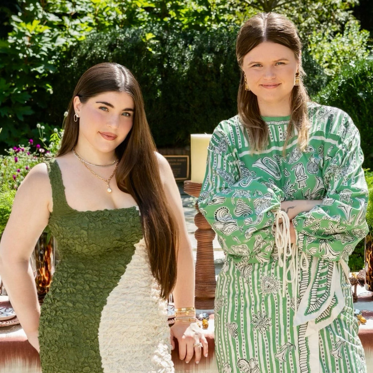 Two women in green dresses standing outdoors with a garden background