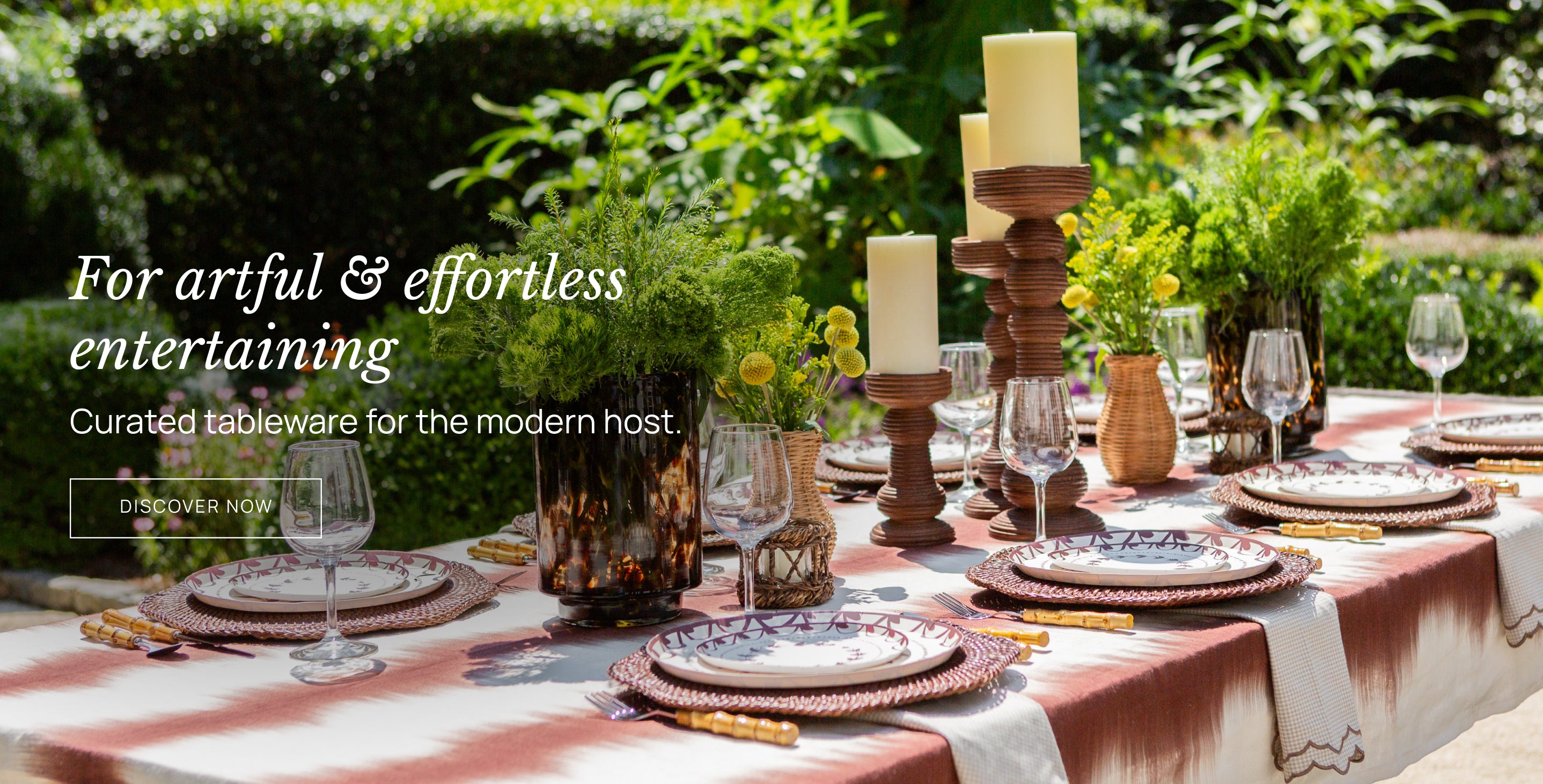 Table setting with candles, glasses, and plates on a checkered tablecloth outdoors.