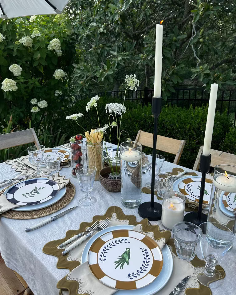 Elegant outdoor table setting with decorative plates, candles, and glasses.