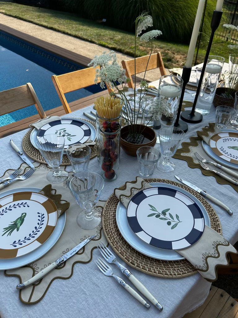Elegant table setting with decorative plates, cutlery, and glasses by a poolside.