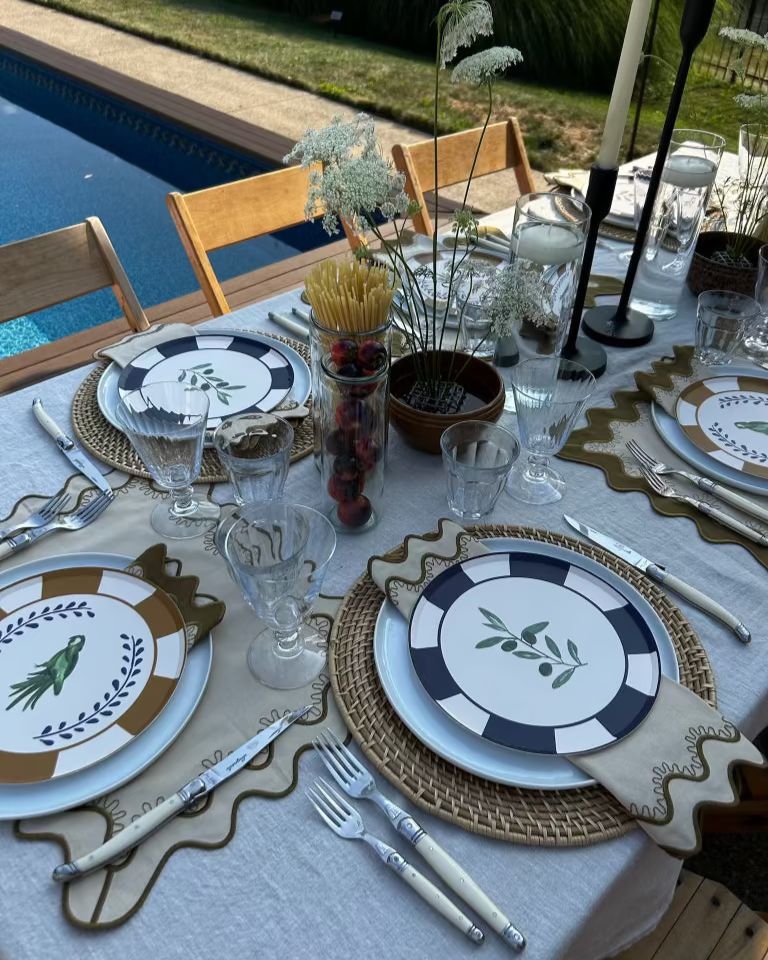 Elegant table setting with decorative plates, glasses, and cutlery by a poolside.