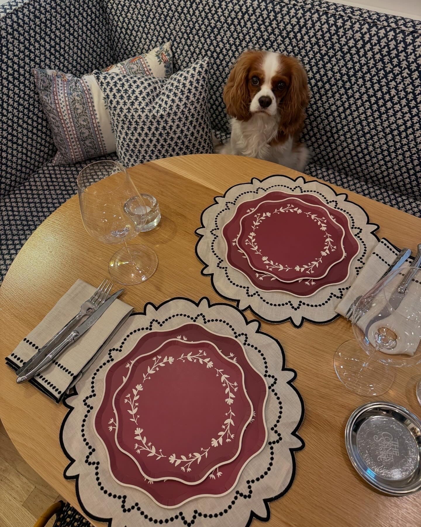 Dog sitting on a couch behind a table set with placemats and glasses.