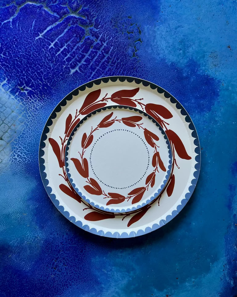 Two stacked paper plates with red leaf design on a blue textured surface