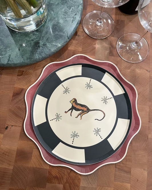 Decorative plate with a monkey design on a wooden table with wine glasses and a glass of water.
