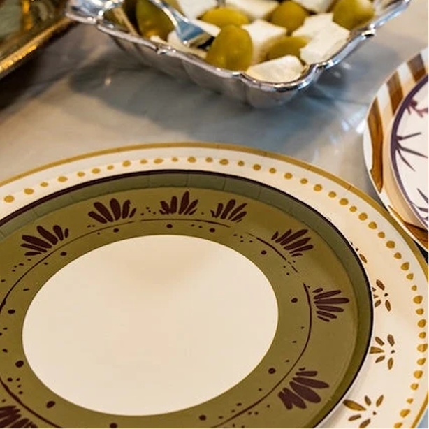 A close-up of a decorative plate with a wide olive green band, dark brown floral motifs, and a cream center, set on a table with other plates and a serving dish in the background.