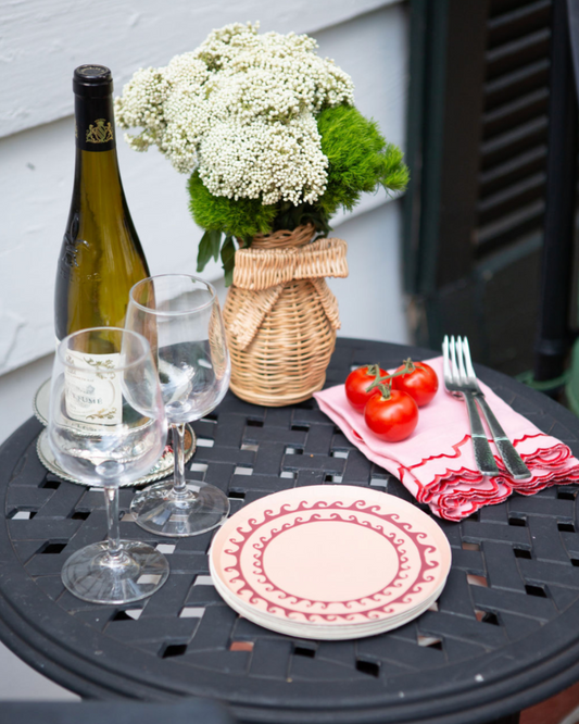 Outdoor table setting with wine, glasses, flowers, and tomatoes.