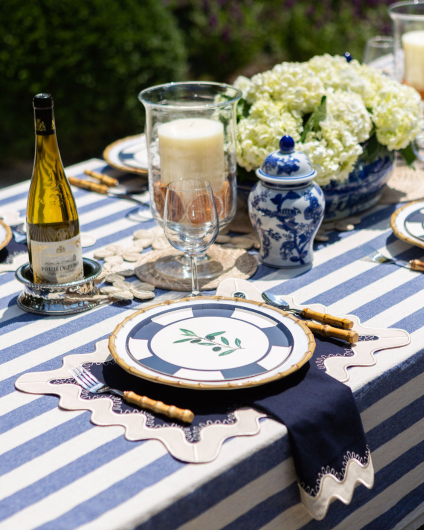 Elegant outdoor table setting with blue and white striped tablecloth, decorative plates, and floral centerpieces.