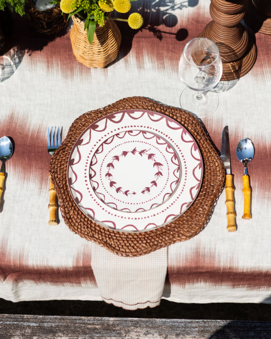Dining table setting with woven placemat, patterned plate, and cutlery on a textured tablecloth.
