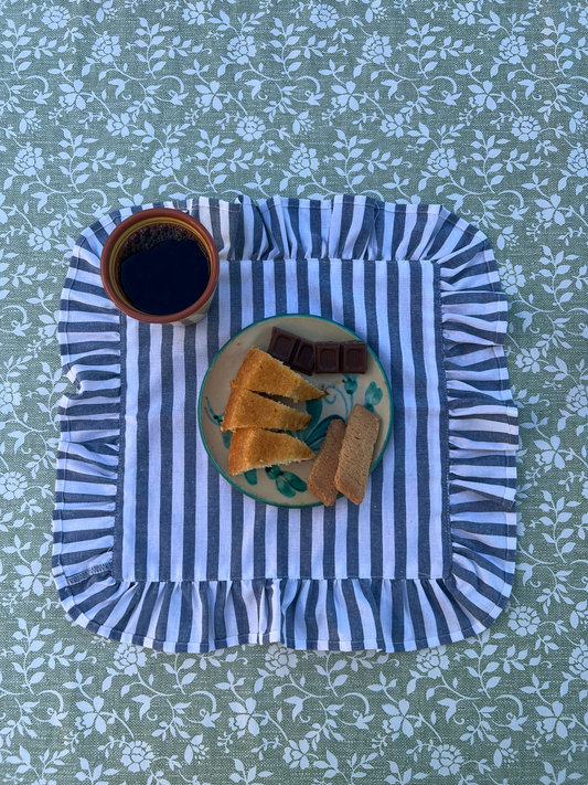 Striped blue and white placemat with a plate of food and cup on a floral tablecloth.