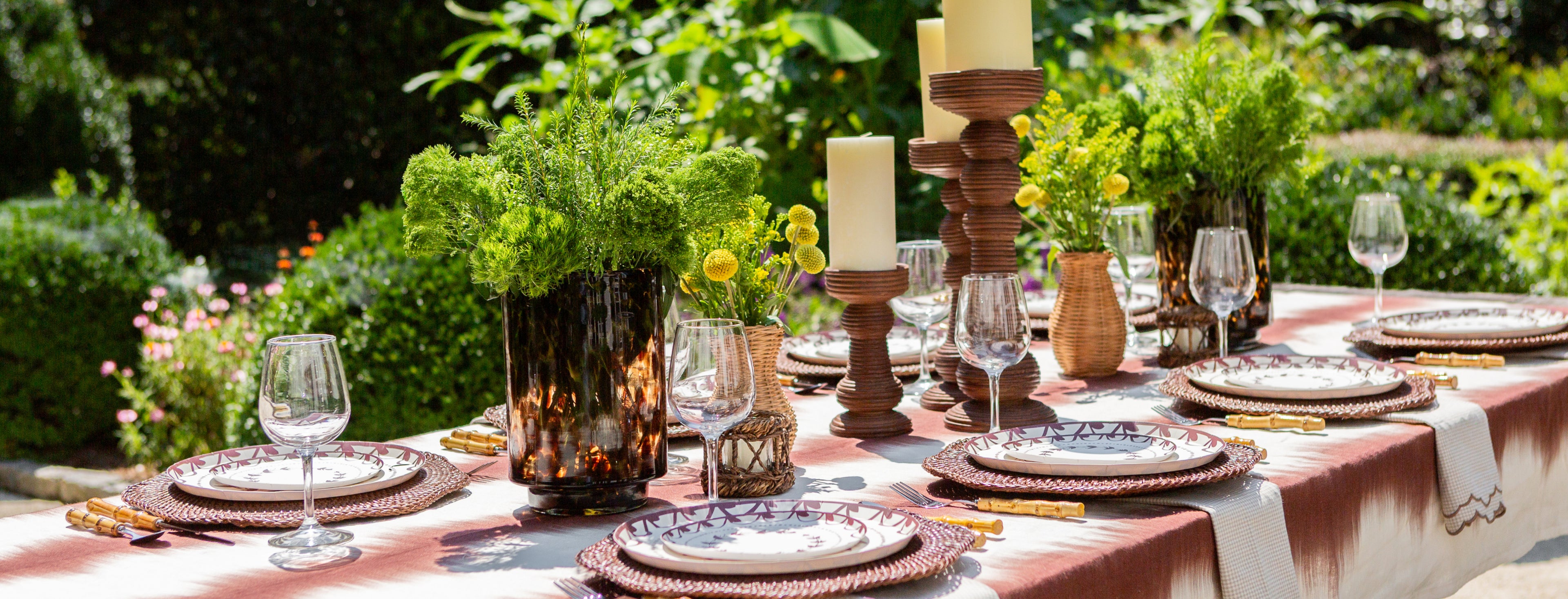an outdoor tablescape with decorative plates vases and candlesticks