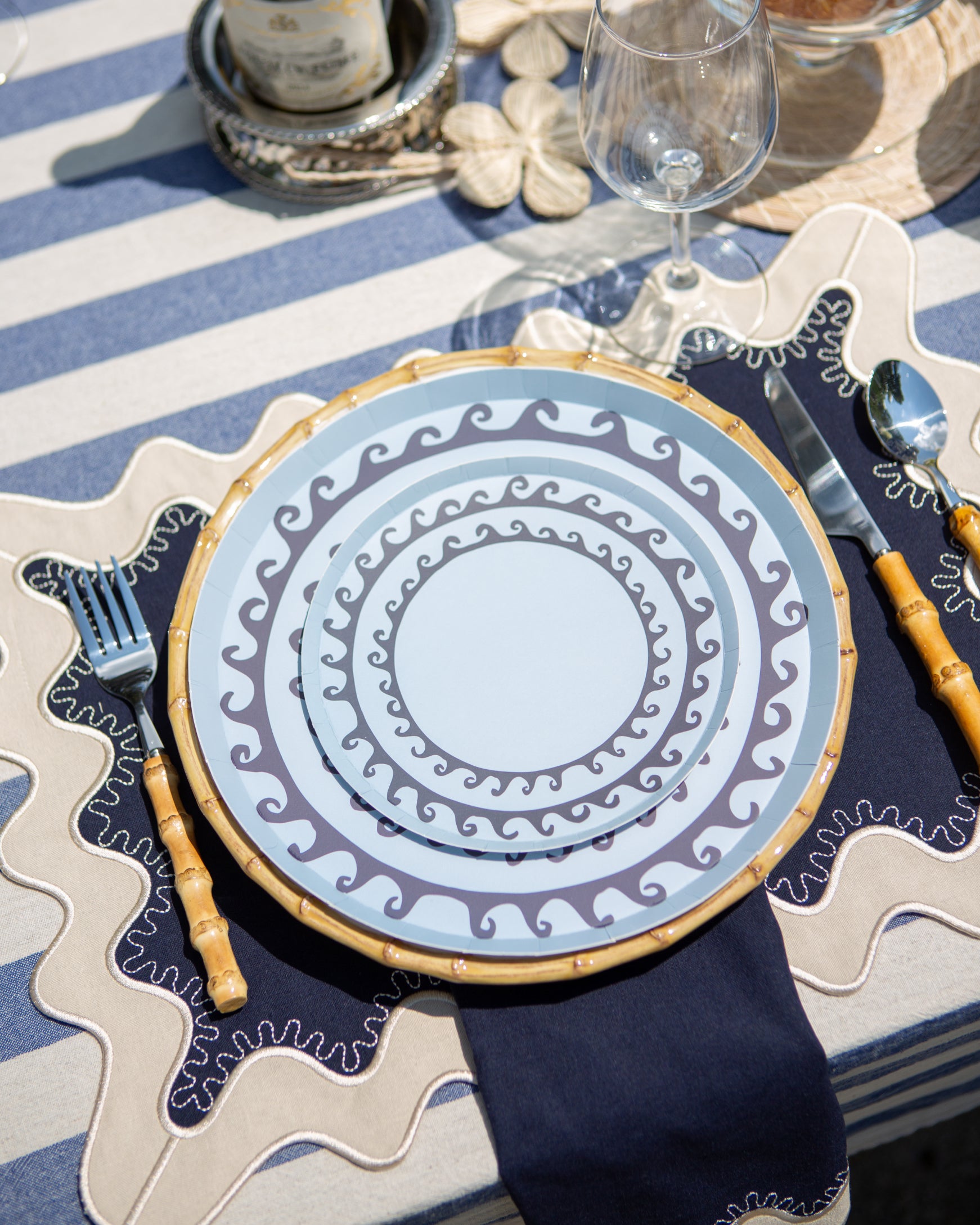 Decorative blue plates with darker blue wave pattern set on a navy blue and white placemat with cutlery