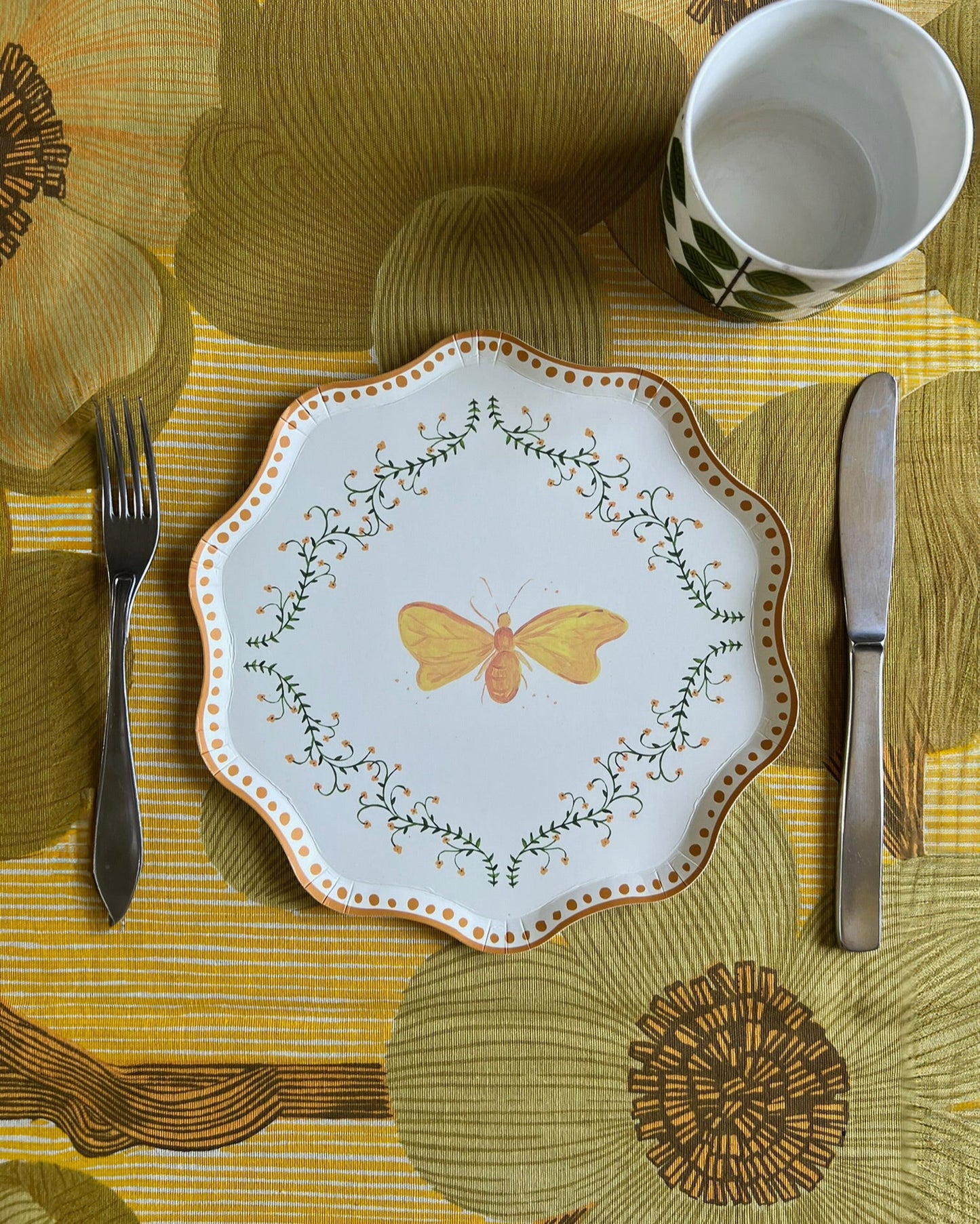 Decorative plate with butterfly design on a table setting with a yellow and brown floral tablecloth.