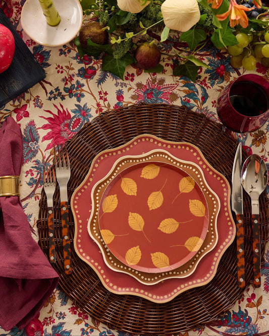 a table with a floral tablecloth red and gold plates and cutlery