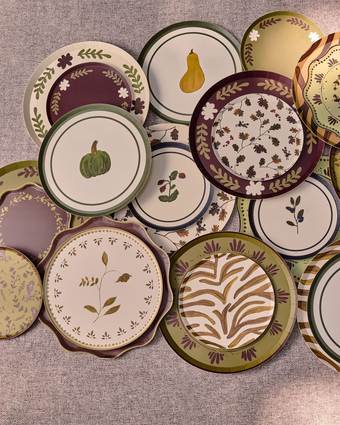 A collection of decorative plates with autumn-themed patterns, including pumpkins, gourds, leaves, and stripes, arranged on a table.