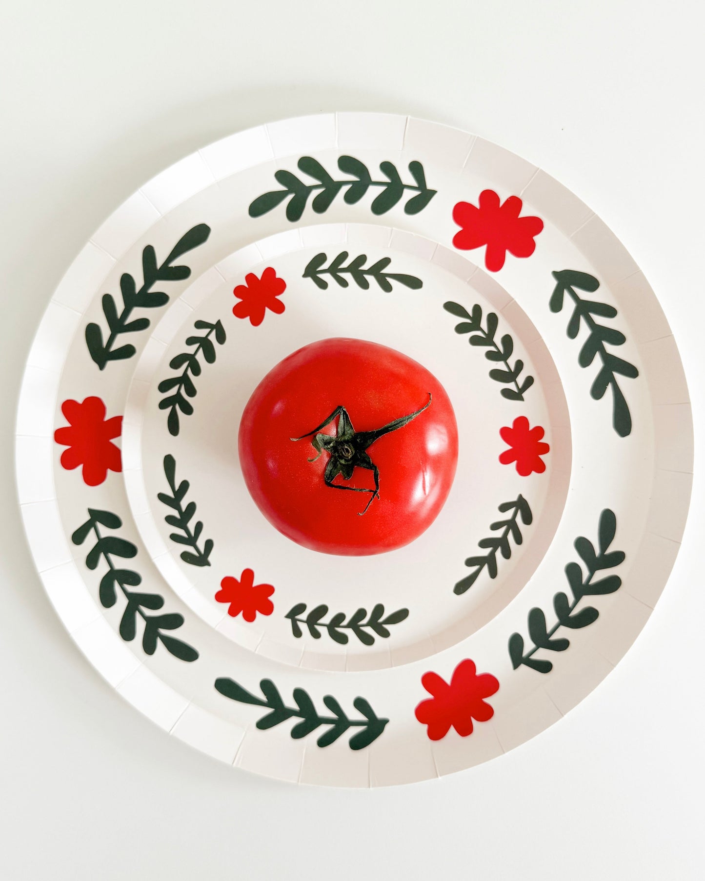 two white plates layered with green and red details and a tomato in the center