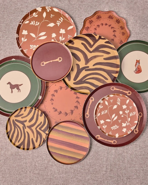 A group of decorative plates in earthy terracotta, brown, green, and beige tones, arranged on a round gray surface outdoors.