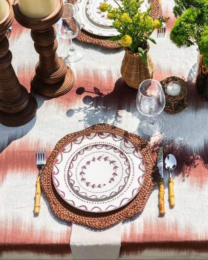 Elegant table setting with decorative plates, cutlery, and candles on a patterned tablecloth.