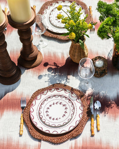 Elegant table setting with woven placemats, glassware, and candles on a textured tablecloth.