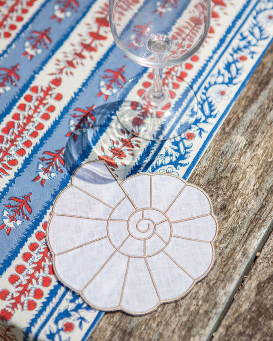 Decorative shell coaster on a table with a patterned tablecloth and wine glass.