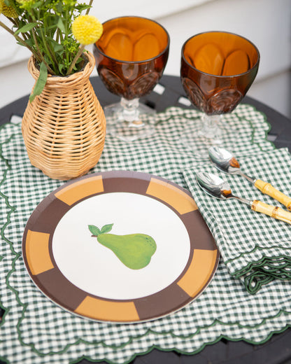 Dining table setting with a plate featuring a pear design, glasses, and cutlery on a checkered placemat