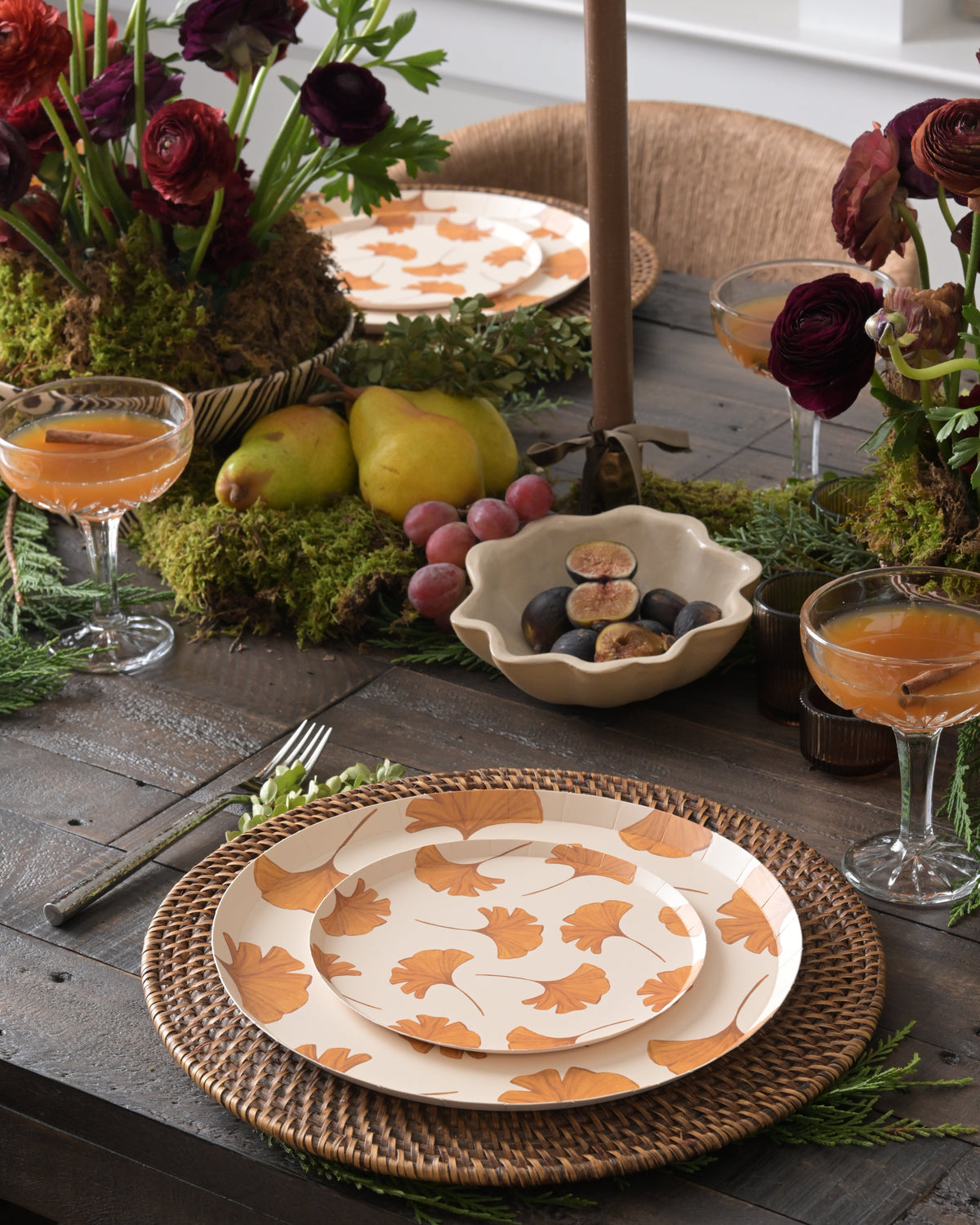a styled table with florals and fruit as the centerpiece. Each place setting has two plates layered with gold leaves. 