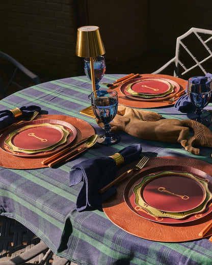 a table setting outdoors with horse themed plates and a blue and green plaidtablecloth 