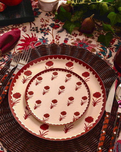 a table set with a floral table cloth and white plates with a red floral pattern