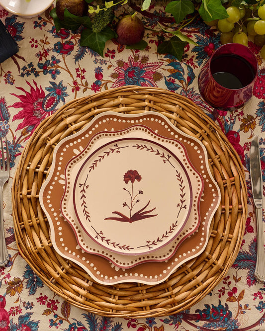 a table setting with a rattan placemat, layered plates with a floral motif in the center.