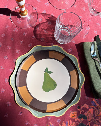 Decorative plate with a pear design on a table with a red tablecloth and glasses.