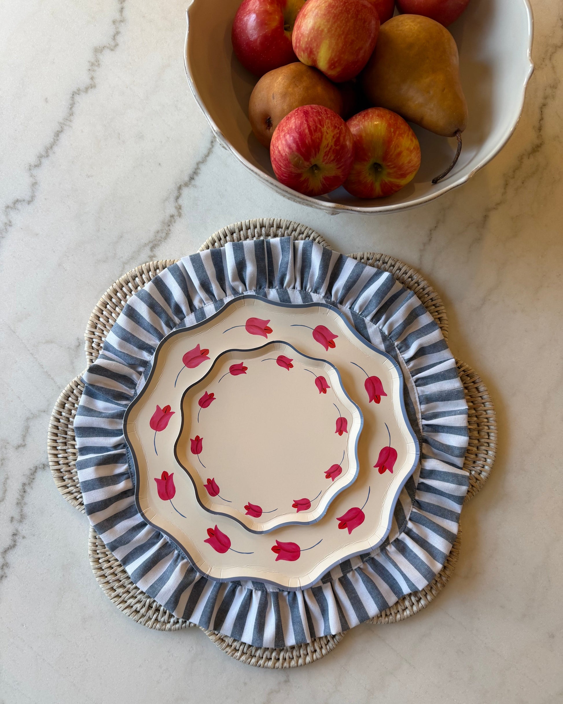 Decorative plate with floral pattern on a marble surface next to a bowl of apples and pears.