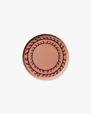 Round pink decorative plate with a maroon wave design 