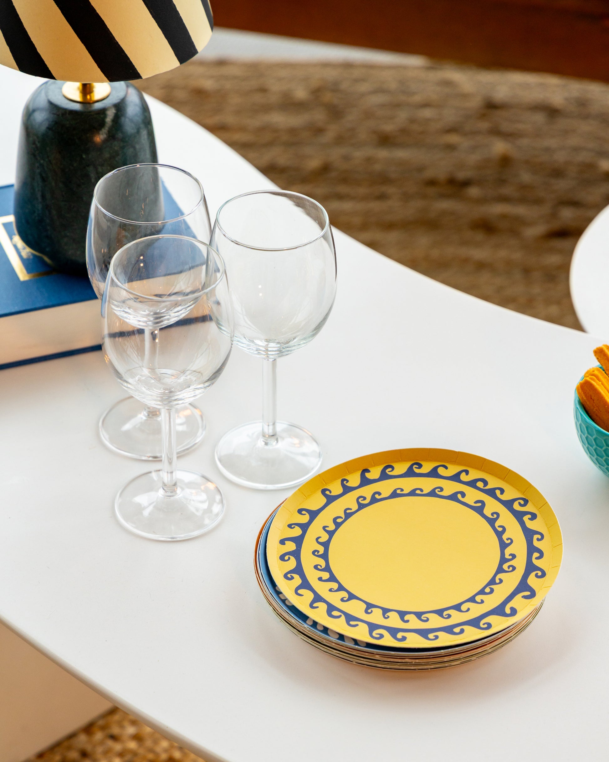A stack of decorative plates on a white table with wine glasses